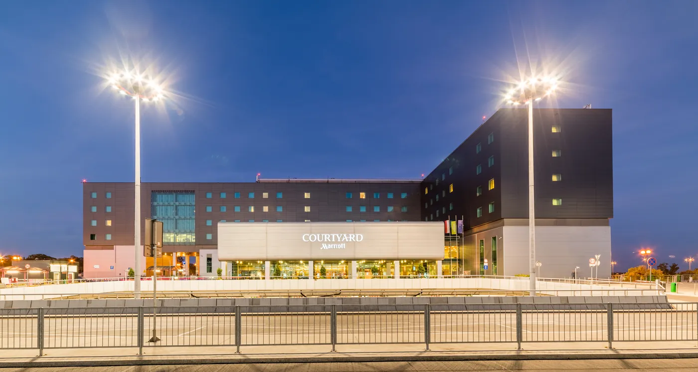 Hotel Courtyard by Marriott Warsaw Airport o zmierzchu &ndash; wejście gł&oacute;wne z podświetlonym logo